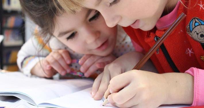 two young kids focusing on writing in a book